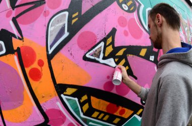 Gri kapüşonlu genç bir adam, yağmurlu havalarda grafiti bir duvar pembe ve yeşil renklerde boyar. Balıkgözü atış