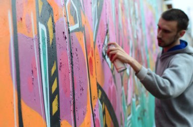 Gri kapüşonlu genç adam duvar ve bulanık sanatçı parçası üzerinde yağışlı havalarda odak grafiti bir duvar pembe ve yeşil renklerde boyalar