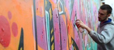 Gri kapüşonlu genç adam duvar ve bulanık sanatçı parçası üzerinde yağışlı havalarda odak grafiti bir duvar pembe ve yeşil renklerde boyalar