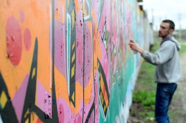 Gri kapüşonlu genç adam duvar ve bulanık sanatçı parçası üzerinde yağışlı havalarda odak grafiti bir duvar pembe ve yeşil renklerde boyalar