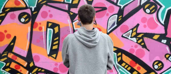 Gri kapüşonlu bir genç grafiti sanatçısı bir duvara yağmurlu havalarda pembe ve yeşil renklerde onun graffiti ile duvara görünüyor. Sokak sanatı kavramı