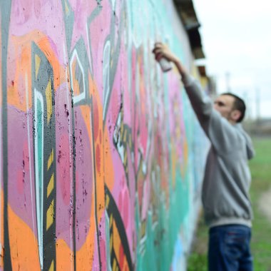 Gri kapüşonlu genç adam duvar ve bulanık sanatçı parçası üzerinde yağışlı havalarda odak grafiti bir duvar pembe ve yeşil renklerde boyalar