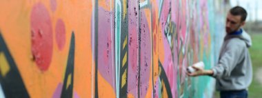 Gri kapüşonlu genç adam duvar ve bulanık sanatçı parçası üzerinde yağışlı havalarda odak grafiti bir duvar pembe ve yeşil renklerde boyalar