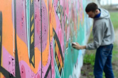 Gri kapüşonlu genç adam duvar ve bulanık sanatçı parçası üzerinde yağışlı havalarda odak grafiti bir duvar pembe ve yeşil renklerde boyalar