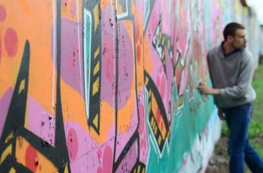Gri kapüşonlu genç adam duvar ve bulanık sanatçı parçası üzerinde yağışlı havalarda odak grafiti bir duvar pembe ve yeşil renklerde boyalar