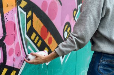 El gri kapüşonlu genç bir adamın grafiti bir duvar pembe ve yeşil renklerde yağmurlu havalarda boyar.
