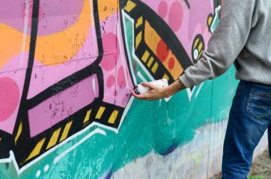 El gri kapüşonlu genç bir adamın grafiti bir duvar pembe ve yeşil renklerde yağmurlu havalarda boyar.