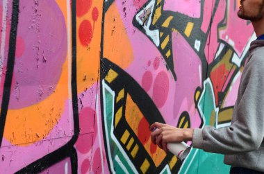 Gri kapüşonlu genç bir adam grafiti bir duvar pembe ve yeşil renklerde yağmurlu havalarda boyar.