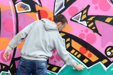 Gri kapüşonlu genç bir adam grafiti bir duvar pembe ve yeşil renklerde yağmurlu havalarda boyar.