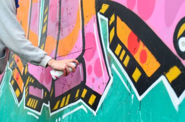 El gri kapüşonlu genç bir adamın grafiti bir duvar pembe ve yeşil renklerde yağmurlu havalarda boyar.