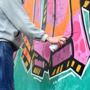 El gri kapüşonlu genç bir adamın grafiti bir duvar pembe ve yeşil renklerde yağmurlu havalarda boyar.