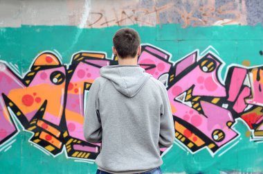 Gri kapüşonlu bir genç grafiti sanatçısı bir duvara yağmurlu havalarda pembe ve yeşil renklerde onun graffiti ile duvara görünüyor. Sokak sanatı kavramı