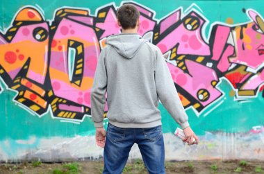 Gri kapüşonlu bir genç grafiti sanatçısı bir duvara yağmurlu havalarda pembe ve yeşil renklerde onun graffiti ile duvara görünüyor. Sokak sanatı kavramı