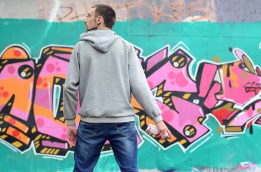 Gri kapüşonlu bir genç grafiti sanatçısı bir duvara yağmurlu havalarda pembe ve yeşil renklerde onun graffiti ile duvara görünüyor. Sokak sanatı kavramı