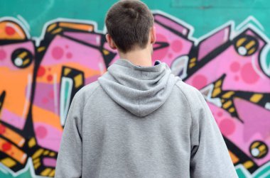 Gri kapüşonlu bir genç grafiti sanatçısı bir duvara yağmurlu havalarda pembe ve yeşil renklerde onun graffiti ile duvara görünüyor. Sokak sanatı kavramı