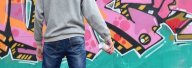 Gri kapüşonlu bir genç grafiti sanatçısı bir duvara yağmurlu havalarda pembe ve yeşil renklerde onun graffiti ile duvara görünüyor. Sokak sanatı kavramı