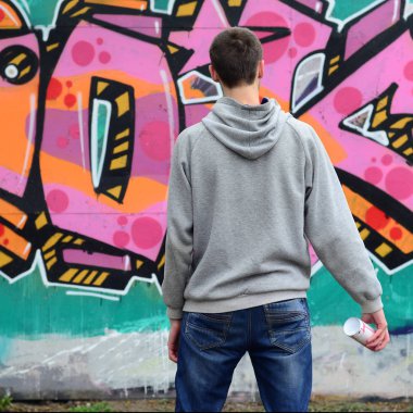 Gri kapüşonlu bir genç grafiti sanatçısı bir duvara yağmurlu havalarda pembe ve yeşil renklerde onun graffiti ile duvara görünüyor. Sokak sanatı kavramı