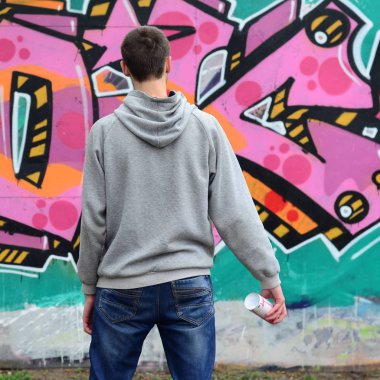 Gri kapüşonlu bir genç grafiti sanatçısı bir duvara yağmurlu havalarda pembe ve yeşil renklerde onun graffiti ile duvara görünüyor. Sokak sanatı kavramı