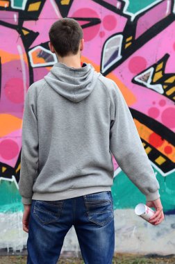 Gri kapüşonlu bir genç grafiti sanatçısı bir duvara yağmurlu havalarda pembe ve yeşil renklerde onun graffiti ile duvara görünüyor. Sokak sanatı kavramı