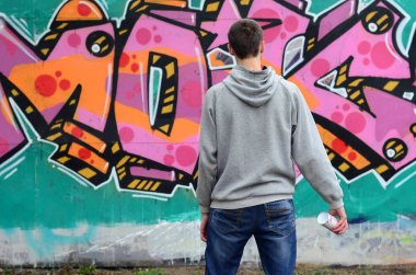 Gri kapüşonlu bir genç grafiti sanatçısı bir duvara yağmurlu havalarda pembe ve yeşil renklerde onun graffiti ile duvara görünüyor. Sokak sanatı kavramı