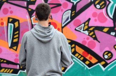 Gri kapüşonlu bir genç grafiti sanatçısı bir duvara yağmurlu havalarda pembe ve yeşil renklerde onun graffiti ile duvara görünüyor. Sokak sanatı kavramı