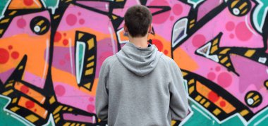Gri kapüşonlu bir genç grafiti sanatçısı bir duvara yağmurlu havalarda pembe ve yeşil renklerde onun graffiti ile duvara görünüyor. Sokak sanatı kavramı