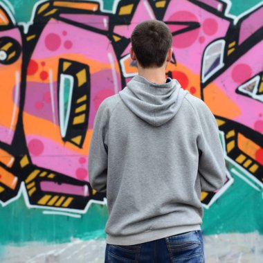 Gri kapüşonlu bir genç grafiti sanatçısı bir duvara yağmurlu havalarda pembe ve yeşil renklerde onun graffiti ile duvara görünüyor. Sokak sanatı kavramı