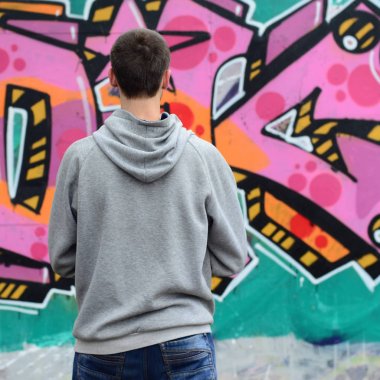 Gri kapüşonlu bir genç grafiti sanatçısı bir duvara yağmurlu havalarda pembe ve yeşil renklerde onun graffiti ile duvara görünüyor. Sokak sanatı kavramı