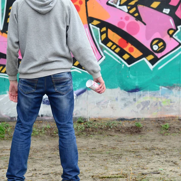 一个穿着灰色上衣的年轻涂鸦艺术家用粉红色和绿色的涂鸦在雨中的墙上看着墙 街道艺术概念 — 图库照片