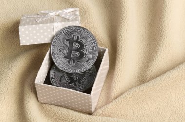 Yumuşak ve kabarık ışık turuncu Polar kumaş çok sayıda kabartma kıvrımları ile yapılmış bir battaniye üzerinde küçük bir yay ile bir küçük turuncu hediye kutusu gümüş bitcoin yatıyor