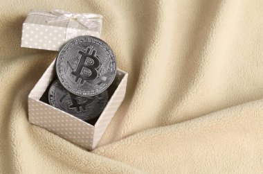 Yumuşak ve kabarık ışık turuncu Polar kumaş çok sayıda kabartma kıvrımları ile yapılmış bir battaniye üzerinde küçük bir yay ile bir küçük turuncu hediye kutusu gümüş bitcoin yatıyor