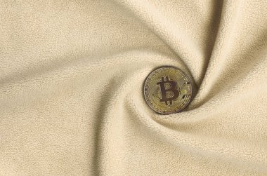 Altın bitcoin yumuşak ve kabarık ışık turuncu Polar kumaş çok sayıda kabartma kıvrımları ile yapılmış bir battaniye yatıyor. Kıvrımları şeklinde bir ekran kartı soğutucu fan benzer