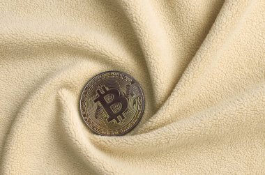 Altın bitcoin yumuşak ve kabarık ışık turuncu Polar kumaş çok sayıda kabartma kıvrımları ile yapılmış bir battaniye yatıyor. Kıvrımları şeklinde bir ekran kartı soğutucu fan benzer