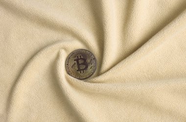 Altın bitcoin yumuşak ve kabarık ışık turuncu Polar kumaş çok sayıda kabartma kıvrımları ile yapılmış bir battaniye yatıyor. Kıvrımları şeklinde bir ekran kartı soğutucu fan benzer