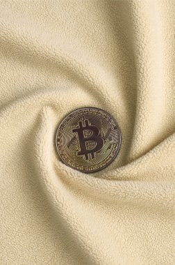 Altın bitcoin yumuşak ve kabarık ışık turuncu Polar kumaş çok sayıda kabartma kıvrımları ile yapılmış bir battaniye yatıyor. Kıvrımları şeklinde bir ekran kartı soğutucu fan benzer