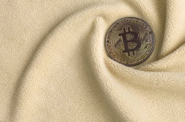 Altın bitcoin yumuşak ve kabarık ışık turuncu Polar kumaş çok sayıda kabartma kıvrımları ile yapılmış bir battaniye yatıyor. Kıvrımları şeklinde bir ekran kartı soğutucu fan benzer