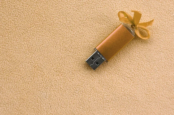 Orange usb flash memory card with a blue bow lies on a blanket of soft and furry light orange fleece fabric. Classic female gift design for a memory card