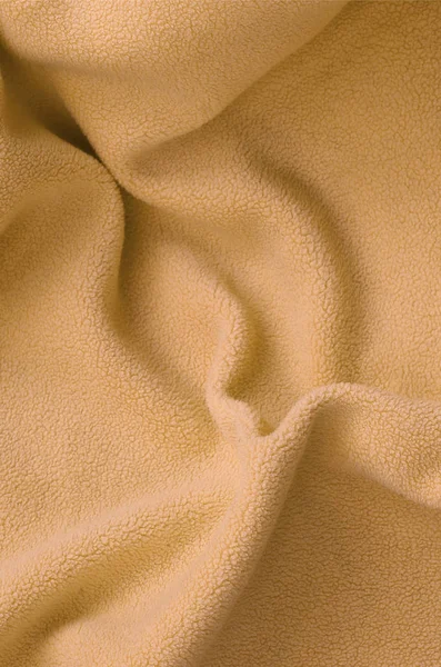 The blanket of furry orange fleece fabric. A background of light orange soft plush fleece material with a lot of relief folds