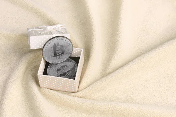 Le Bitcoin argent se trouve dans une petite boîte-cadeau orange avec un petit noeud sur une couverture faite de doux et moelleux tissu polaire orange clair avec un grand nombre de plis en relief — Photo