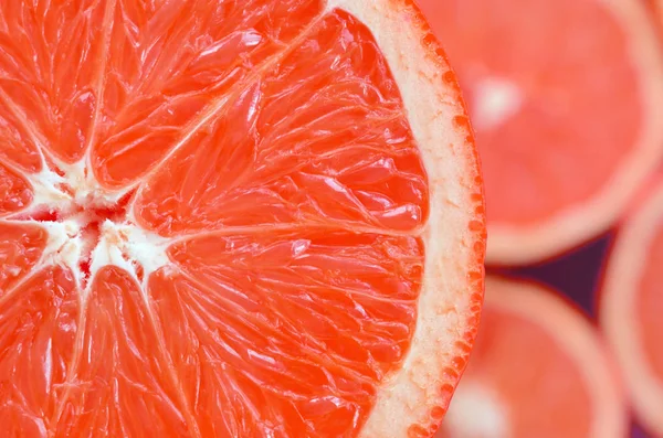 Top view of a fragment of the red grapefruit slice on the background of many blurred grapefruit slices. A saturated citrus texture image