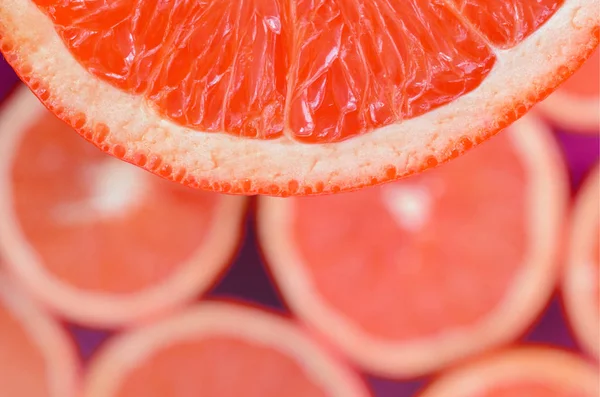 Top view of a fragment of the red grapefruit slice on the background of many blurred grapefruit slices. A saturated citrus texture image