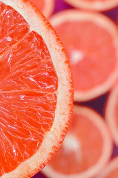 Top view of a fragment of the red grapefruit slice on the background of many blurred grapefruit slices. A saturated citrus texture image