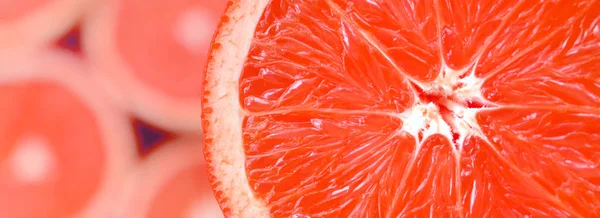 Top view of a fragment of the red grapefruit slice on the background of many blurred grapefruit slices. A saturated citrus texture image