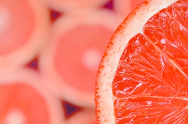 Top view of a fragment of the red grapefruit slice on the background of many blurred grapefruit slices. A saturated citrus texture image