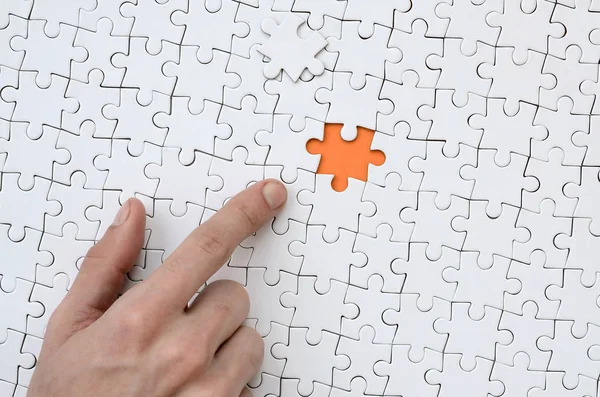 一个白色拼图的纹理在组装状态与一个缺失的元素 形成一个橙色的空间 指着男性的手指着 — 图库照片