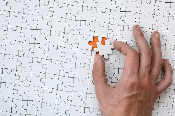 La trama di un puzzle bianco nello stato assemblato con un elemento mancante che la mano maschile inserisce — Foto Stock