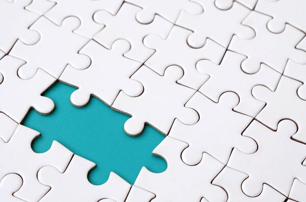 Close-up texture of a white jigsaw puzzle in assembled state with missing elements forming a green pad for text. Copy space