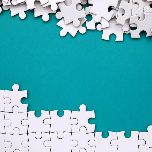 Fragment of a folded white jigsaw puzzle and a pile of uncombed puzzle elements against the background of a blue surface. Texture photo with space for text