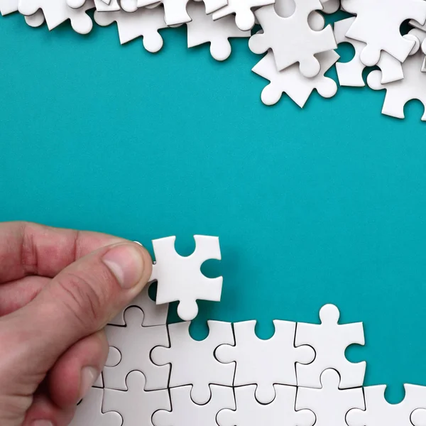 Ruky složí bílé puzzle a hromadu neučesané puzzle kousky leží na pozadí modré povrchu. Foto textur s prostorem pro text — Stock fotografie