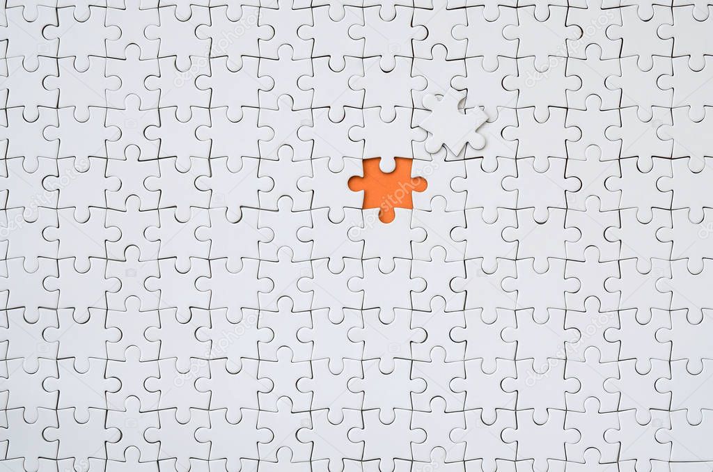 The texture of a white jigsaw puzzle in an assembled state with one missing element forming an orange space
